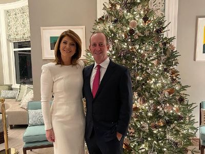 Norah O'Donnell and Geoff Tracy are posing Infront of a Christmas tree.